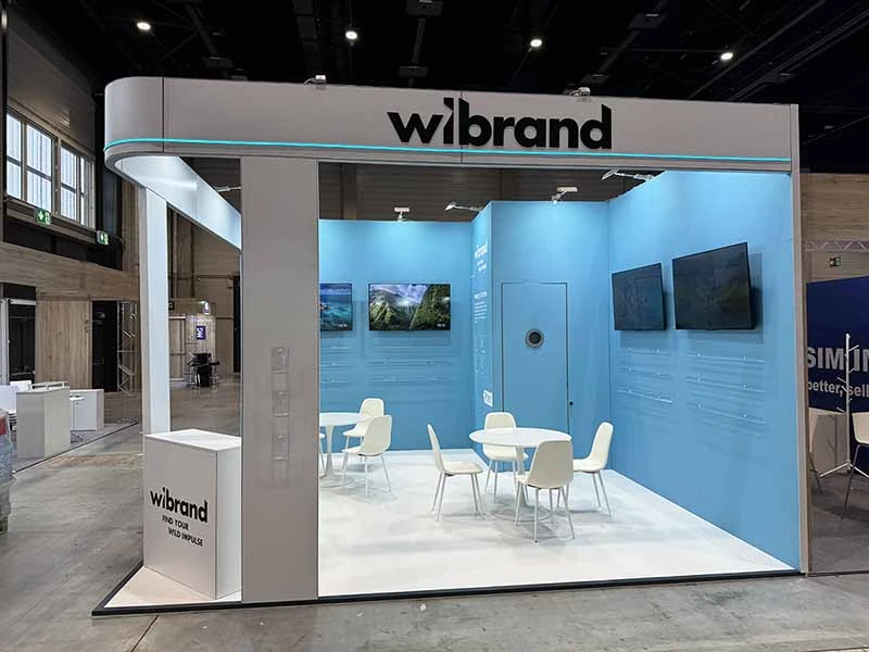 Fertiggestellter Wibrand-Messestand mit blauen Markenflächen, Bildschirmen, Empfangstheke und Besprechungsmöbeln